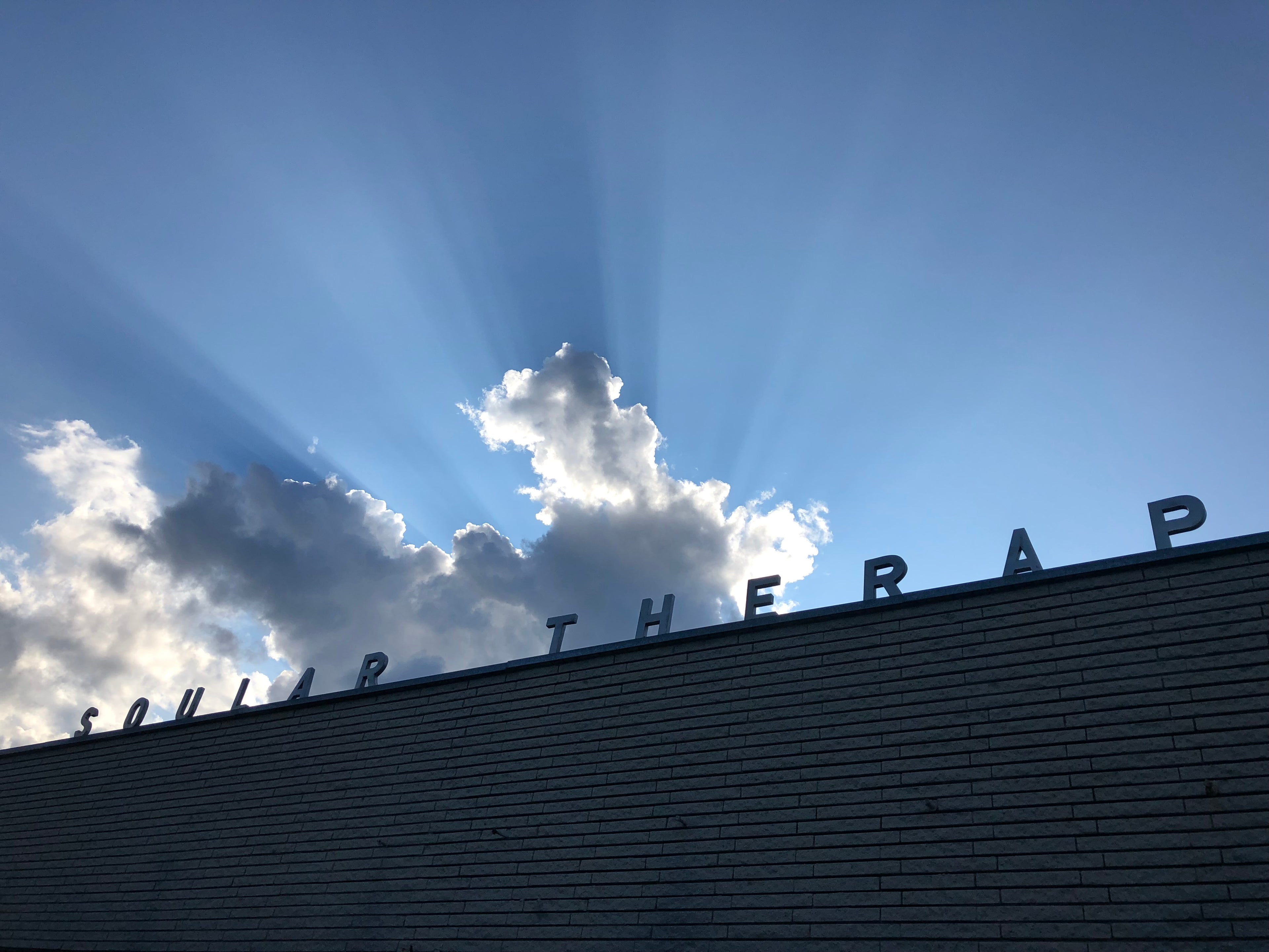 Building with 'Solar Therapy' sign against a blue sky with clouds